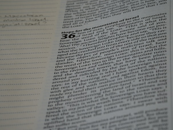 A page from a book with text that appears to be from the Bible. The text is partially in focus and discusses a prophecy to the mountains of Israel. Notes are handwritten in the margin on the left side of the page.