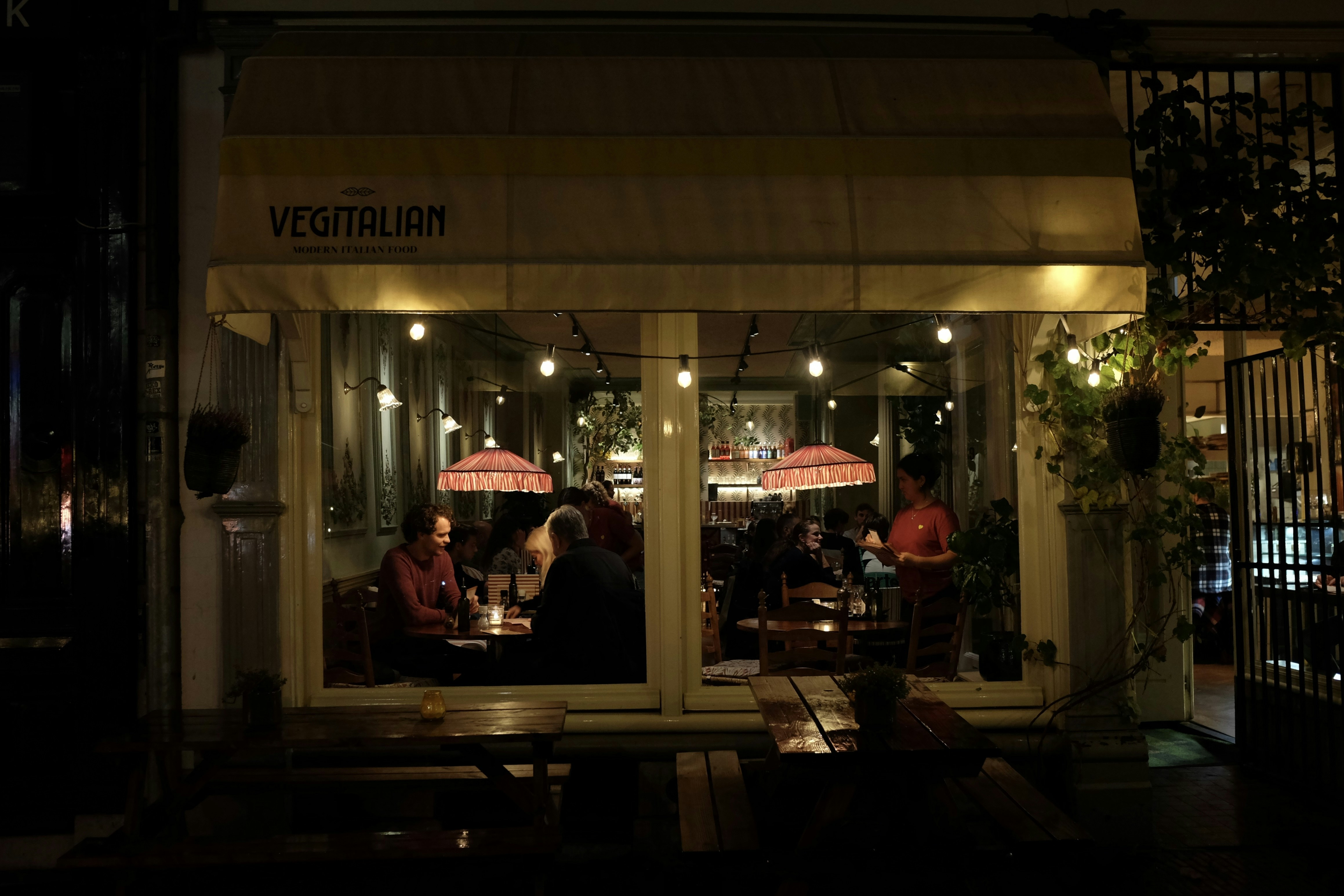 a group of people sitting outside of a restaurant at night