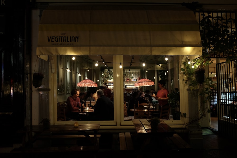 a group of people sitting outside of a restaurant at night