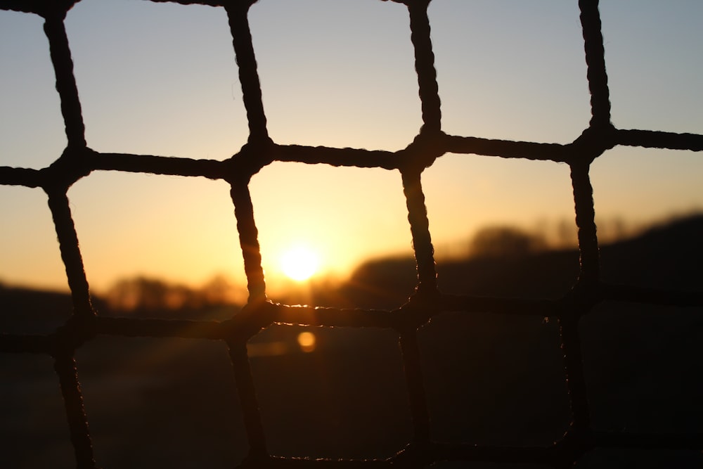 the sun is setting behind a wire fence