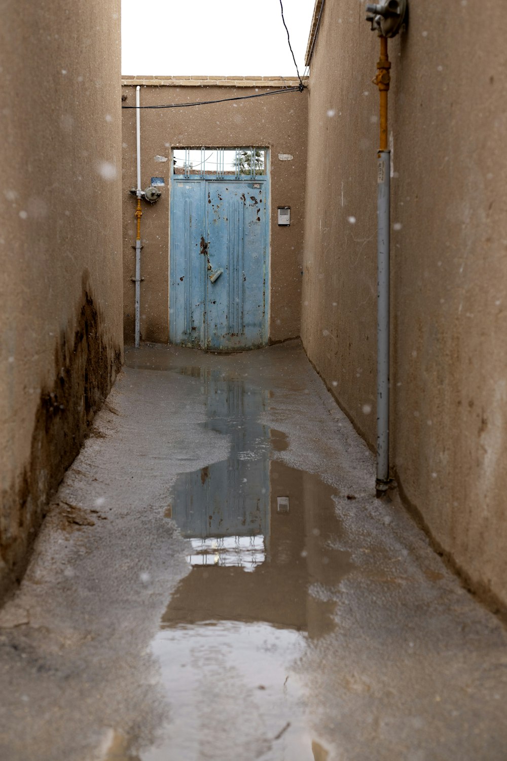 a narrow hallway with a blue door and pipes