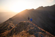 Sunset casting golden light over a mountain ridge with hikers silhouetted.