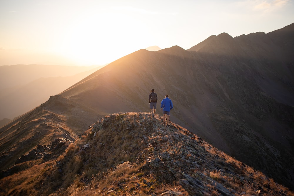 two people standing on top of a mountain at sunset
