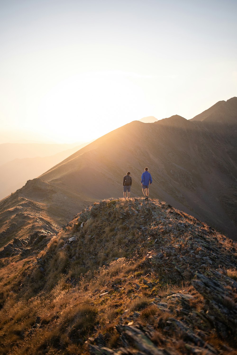 two people walking up a hill at sunset