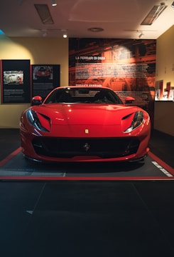 A Ferrari gleaming under soft spotlight, its red curves vivid against the dark showroom background