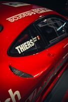 A red sports car with black details featuring a window with decals including the word 'THIERS' and a small flag. The car body displays the words 'SCUDERIA' above the window.