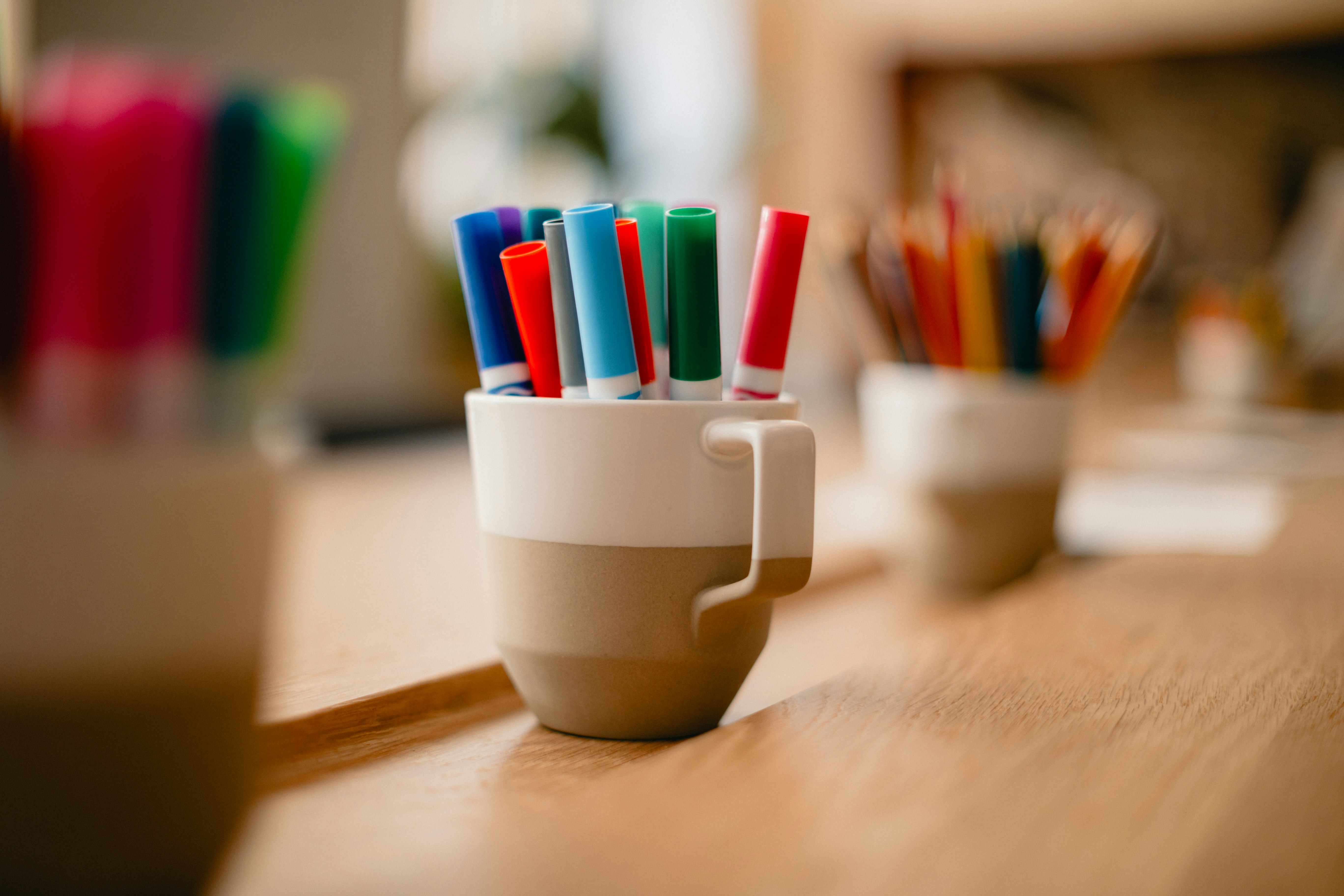 a coffee cup filled with colorful markers on top of a wooden table