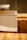 A modern wooden cabinet with straight lines and a light wood finish is partially illuminated by sunlight coming through a window. The light creates distinct shadows across the cabinet and the hardwood floor beneath it.