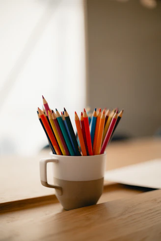 a cup filled with colored pencils sitting on top of a wooden table