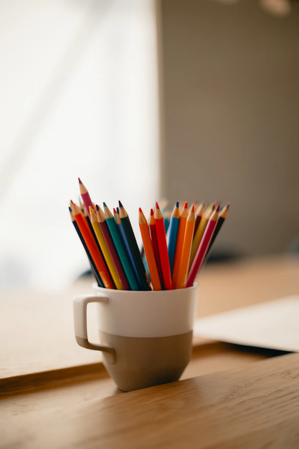 a cup filled with colored pencils sitting on top of a wooden table