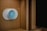 A modern, circular smart thermostat is mounted on a wooden wall. The device displays a message suggesting setup with Wi-Fi and shows the number 50, indicating an indoor temperature setting. The design appears sleek and minimalist.