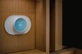 A modern, circular smart thermostat is mounted on a wooden wall. The device displays a message suggesting setup with Wi-Fi and shows the number 50, indicating an indoor temperature setting. The design appears sleek and minimalist.