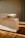A modern, minimalist wooden cabinet with clean, sharp lines and a light wood finish. The cabinet is placed on a hardwood floor, with soft, natural light casting gentle shadows, enhancing the warm tones of the wood.