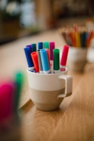 An assortment of pens and markers displayed in a rustic cup on a white table.