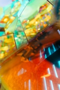 A vibrant and abstract composition featuring reflections and refractions through colorful glass or acrylic panels. The overlapping panels create a kaleidoscope effect with hues of green, blue, and orange. The image has a modern and artistic aesthetic with a play of light and shadows.