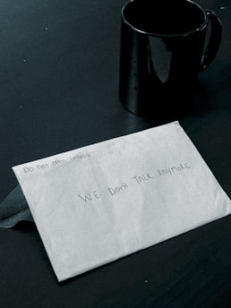 A closed envelope with handwritten text saying 'Do not open unless we don't talk anymore' next to a black coffee mug on a dark surface.