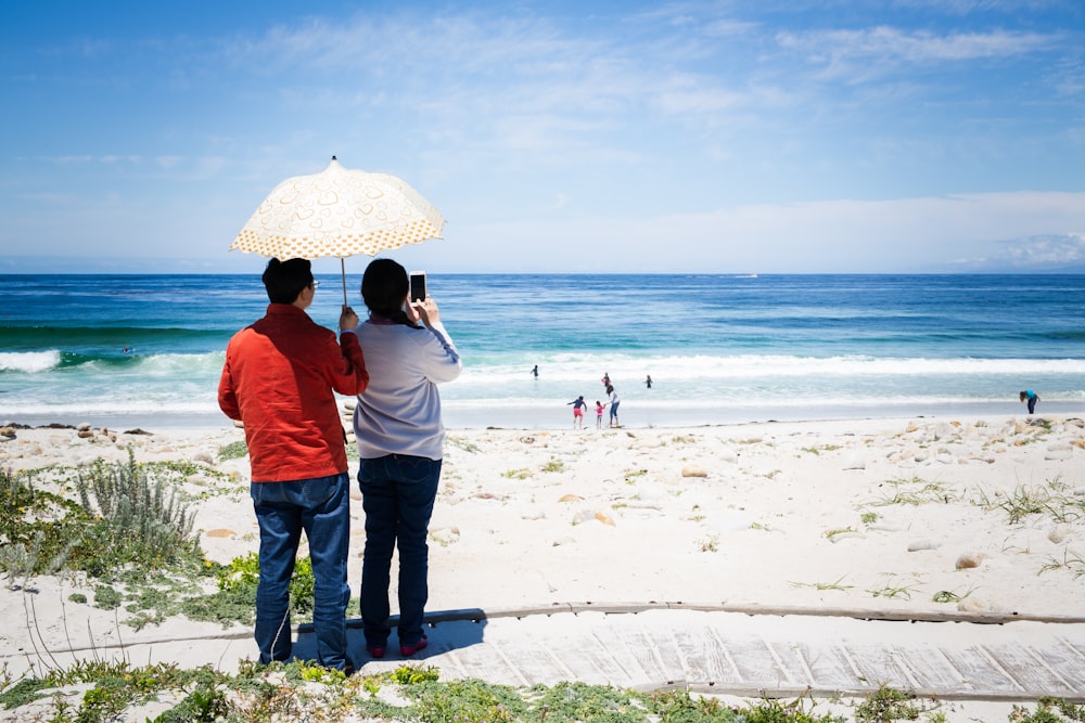 a man and woman standing under an umbrella on the beach