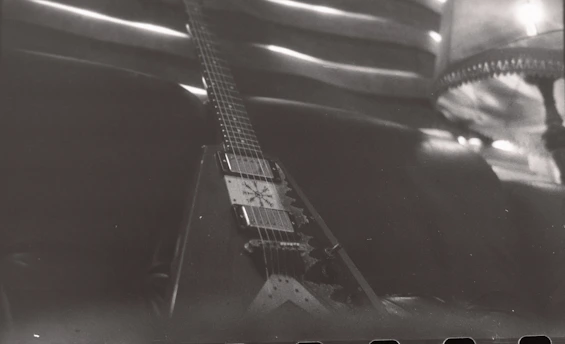 A sleek electric guitar resting against a deep blue velvet backdrop, illuminated by soft noir lighting.