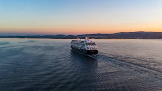 A majestic cruise ship sailing past a stunning coastal landscape at sunset.