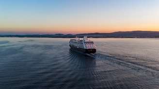 A cruise ship sailing near a scenic coastline at sunset.