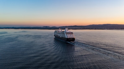 A luxury cruise ship sailing near a scenic coastline at sunset.
