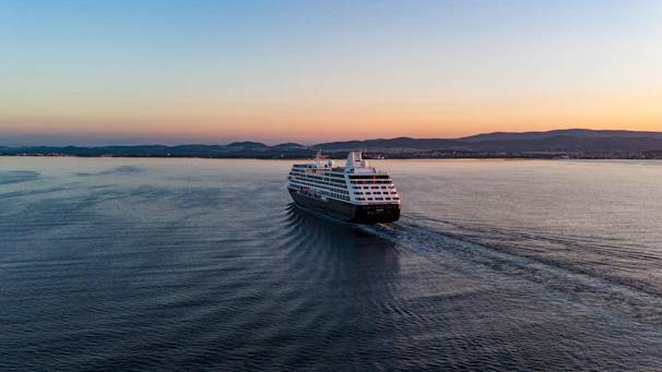 Elegant cruise ship sailing at sunset with calm sea and vibrant sky.