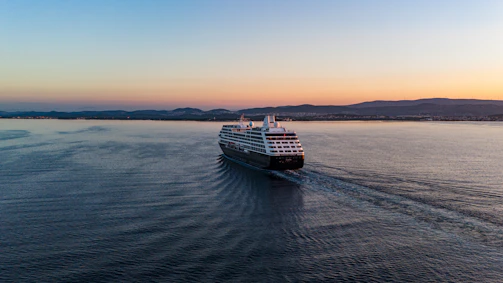 Luxurious cruise ship sailing under a golden sunset over calm blue ocean waters.