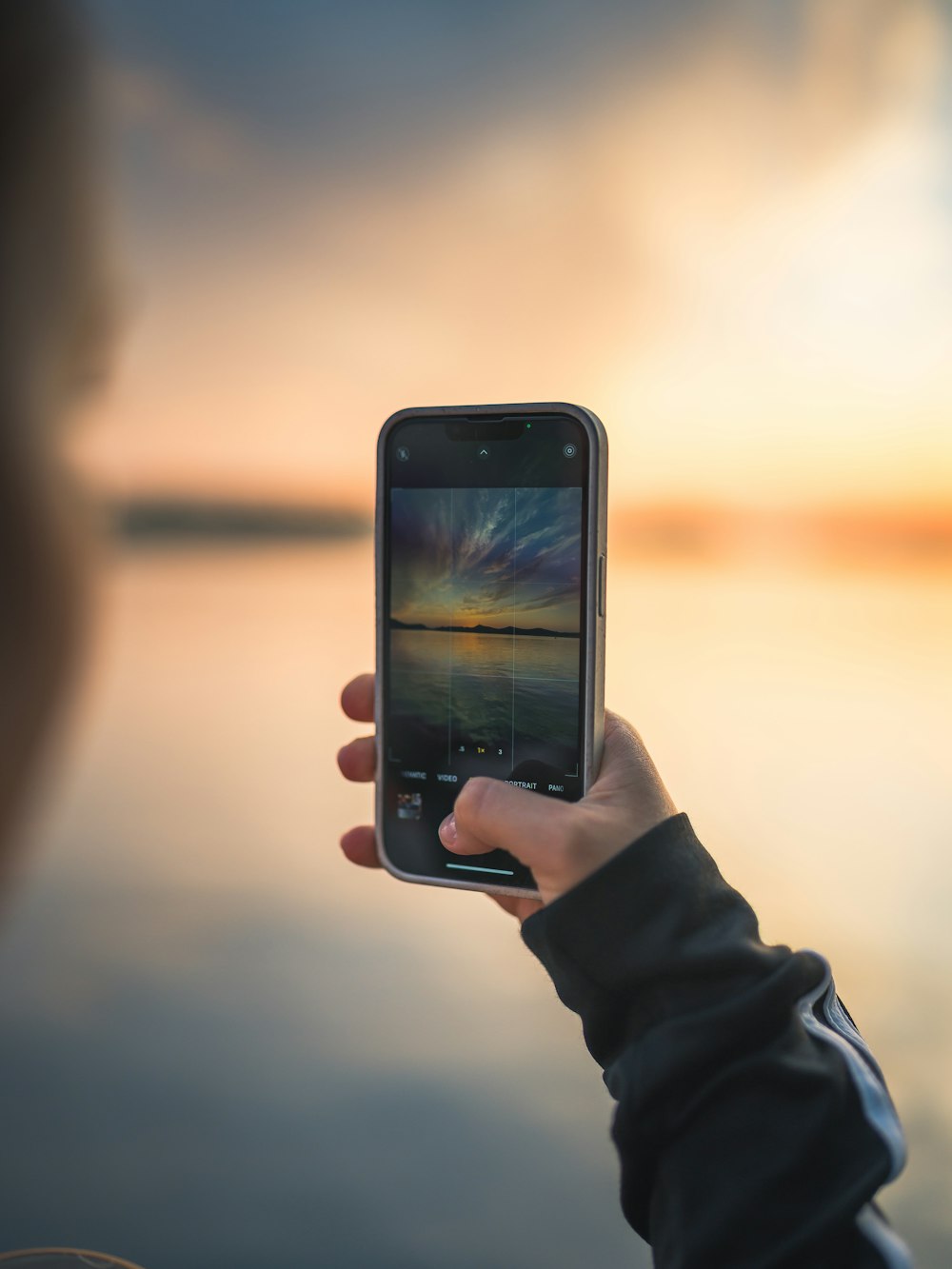 a person holding up a cell phone in front of a body of water