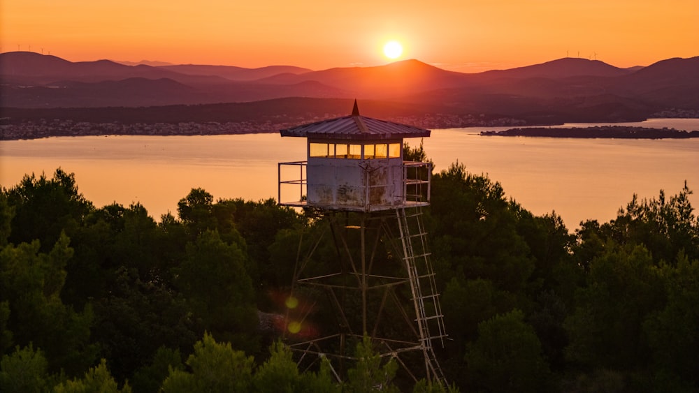 the sun is setting over a lake and a tower