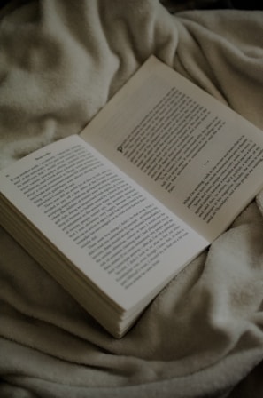 An open book with pages gently turning, resting on a beige linen cloth with olive accents.