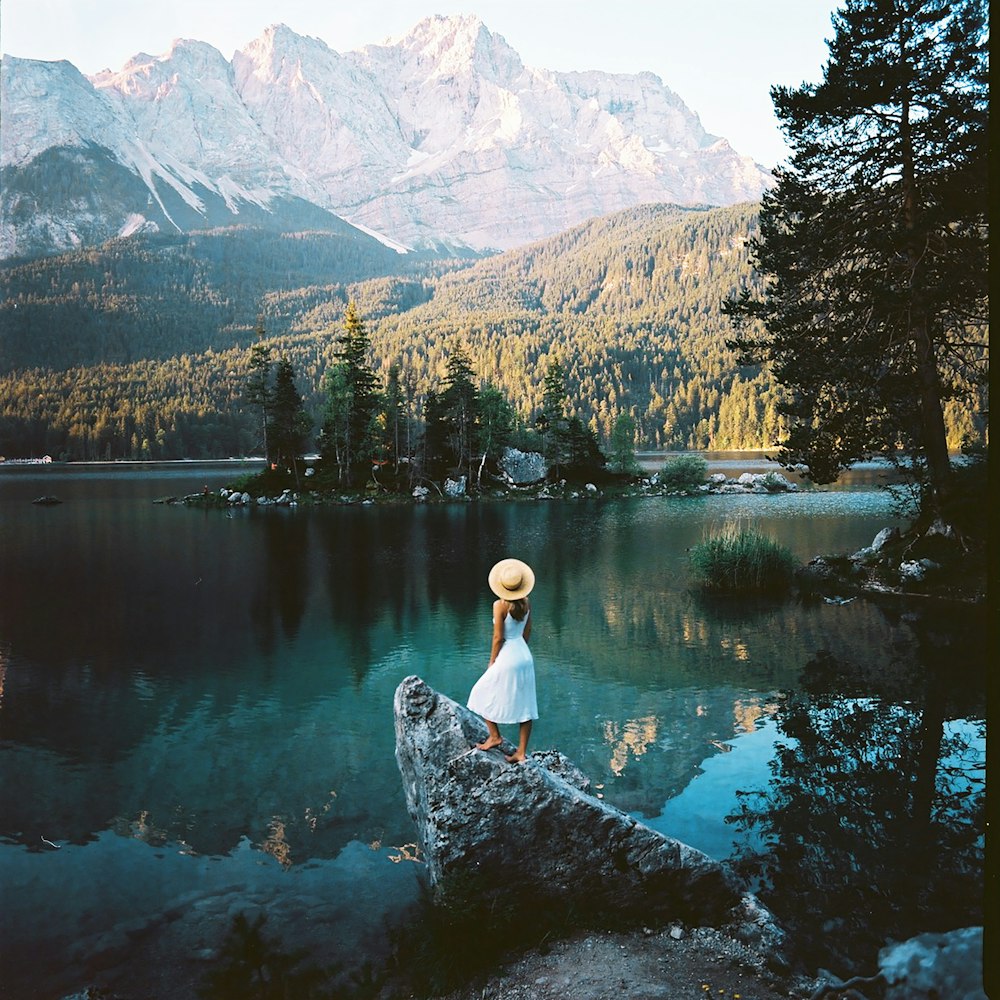 une femme dans un chapeau debout sur un rocher au bord d’un lac