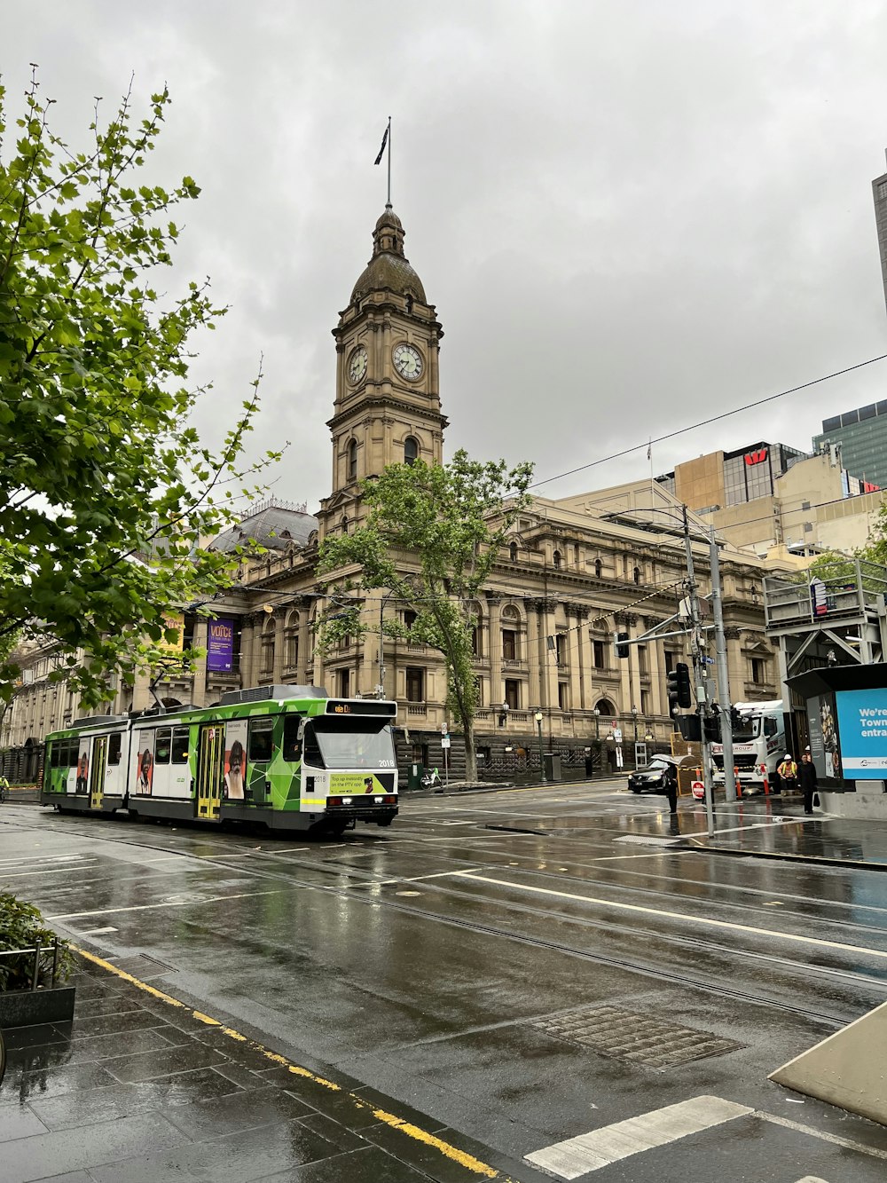 a green and white bus driving down a street next to a tall building