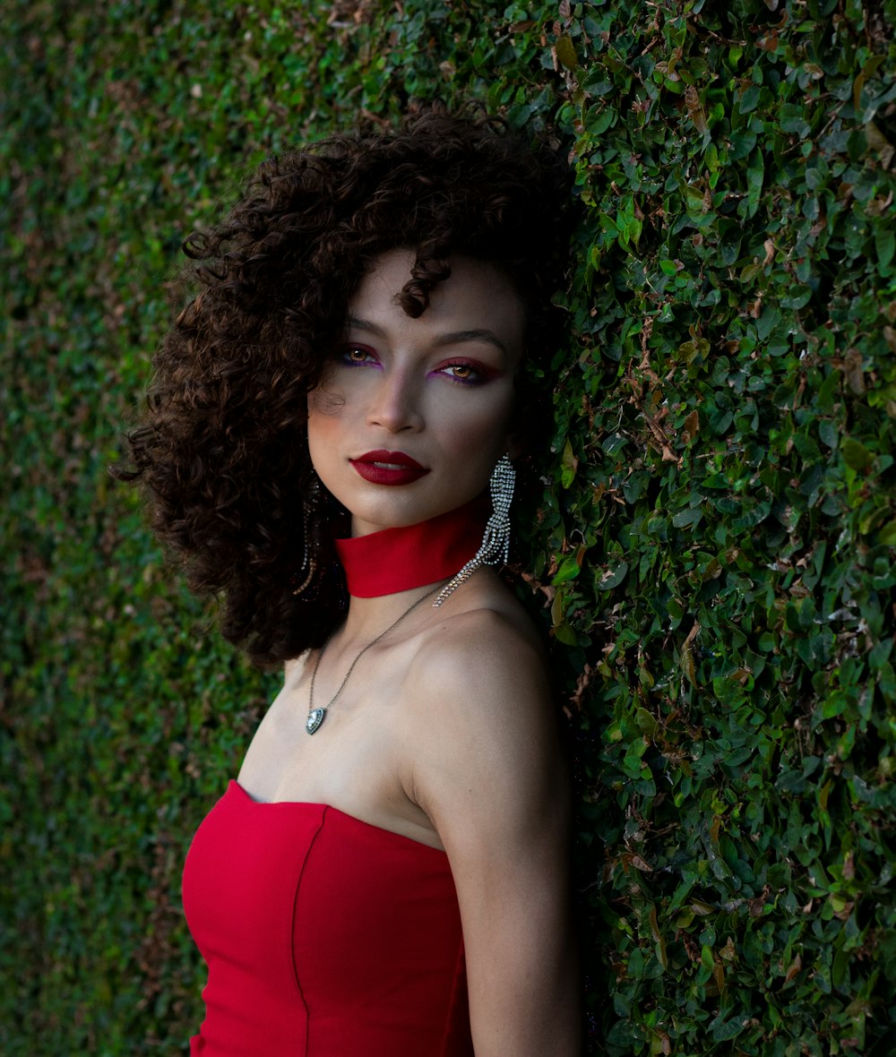 a woman in a red dress leaning against a green wall