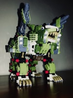 A robotic toy resembling a mechanical creature with sharp teeth, claws, and missile launchers on its back. It has a predominantly green body with white and gold detailing and some red accents. The design is intricate, featuring various mechanical components and joints.