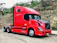 Photo of a smiling truck driver standing beside a Redx Transport semi-truck at sunrise.