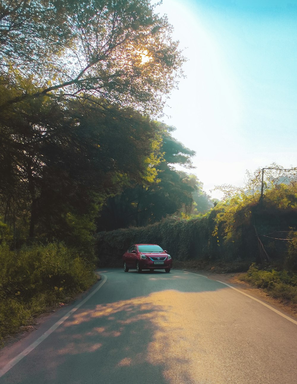 a red car driving down a tree lined road