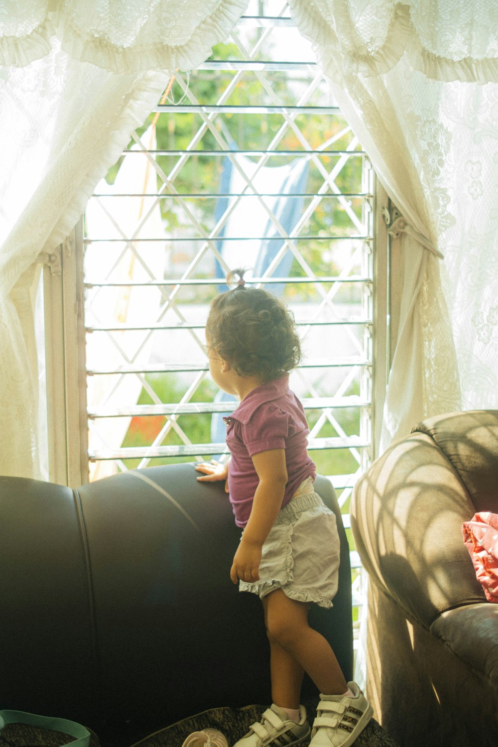 a little girl standing on a couch looking out a window