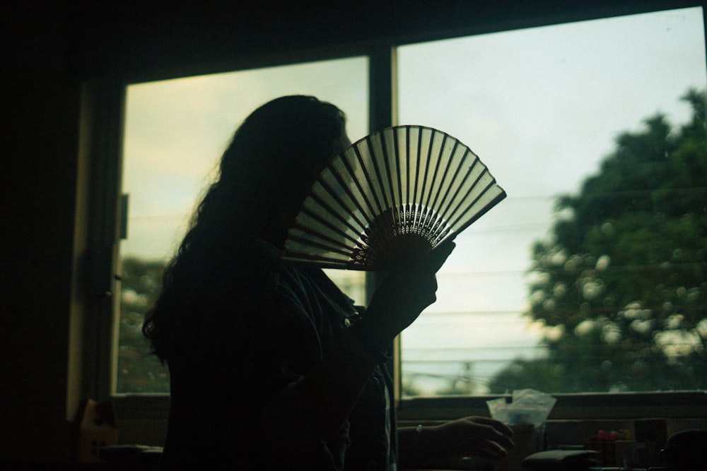 a woman holding a fan in front of a window