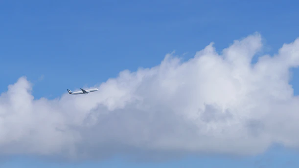 An airplane soaring above fluffy clouds under a bright blue sky, symbolizing the spirit of travel and adventure.