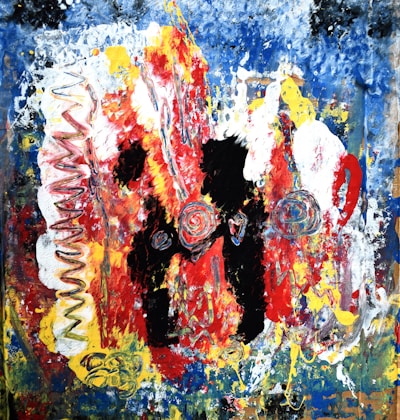 Abstract painting featuring a chaotic blend of colors and textures. Bold red and black swirls are prominent in the center, surrounded by splashes of blue, yellow, and white. The composition includes spiral and zigzag patterns, creating a vibrant and dynamic effect.