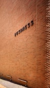 A large brick wall with the word 'BUSINESS' prominently displayed in black letters. The wall is lit by natural daylight, casting gentle shadows along its surface. The ground at the base of the wall has some patches of grass and is bordered by a concrete sidewalk. There are three metal fixtures attached to the lower part of the wall.