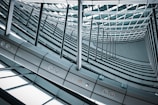An intricately designed interior features a spiraling array of metallic beams and glass panels forming a geometric pattern. The vantage point captures the convergence of lines and curves, creating a sense of depth and perspective within a modern architectural space.