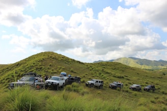 A group of friends enjoying an off-road trip, smiling beside their vehicles under a wide blue sky.