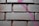 Rectangular bricks with a rough texture are arranged in a neat pattern. A streak of pink spray paint crosses over several bricks, adding a vibrant contrast to the muted color of the bricks.
