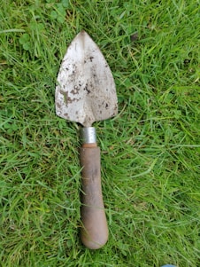 A close-up of hands holding a well-used gardening trowel with fresh soil and green plants in the background.