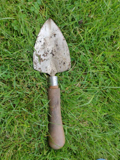 A sturdy garden trowel with a wooden handle placed on fresh soil.