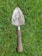 Close-up of a high-carbon steel garden trowel with a comfortable wooden grip resting on soil.