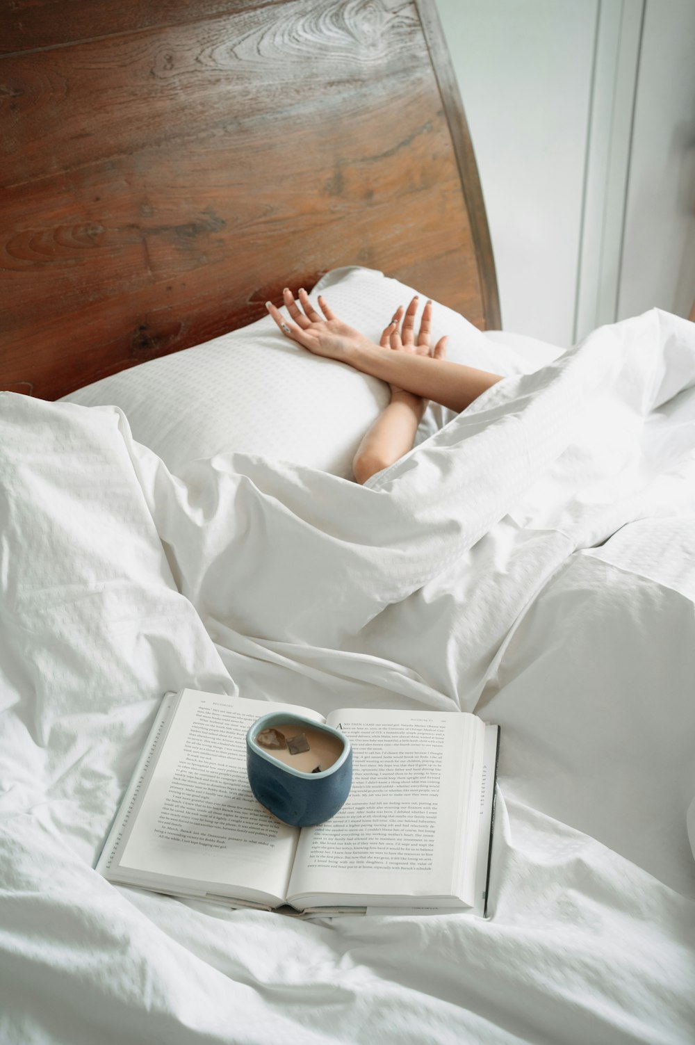 uma pessoa deitada na cama com um livro e uma xícara de café