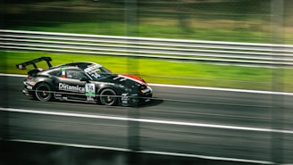 A sleek black race car is speeding down a racetrack, captured in motion, with blurred lines in the background. The car is adorned with various sponsor logos and has the number 14 prominently displayed. The scene conveys a sense of speed and intensity.