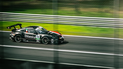 A sleek black race car is speeding down a racetrack, captured in motion, with blurred lines in the background. The car is adorned with various sponsor logos and has the number 14 prominently displayed. The scene conveys a sense of speed and intensity.